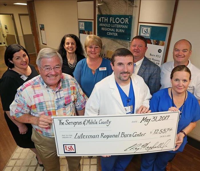 group of men and women smiling for camera holding big check made out to USA Hospital